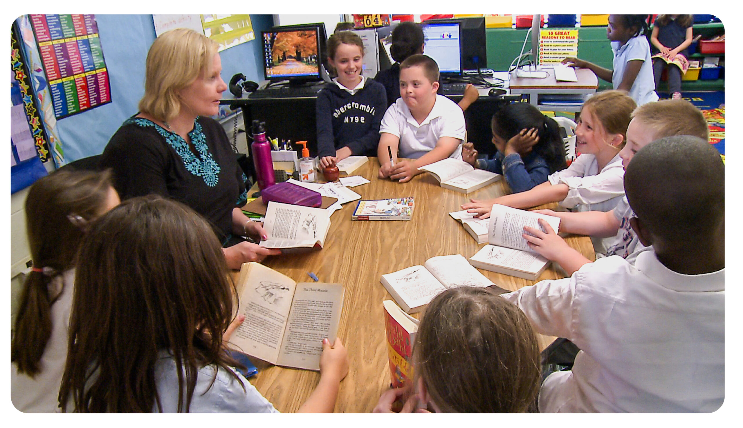 Teacher show a book to students while they sit at a table.